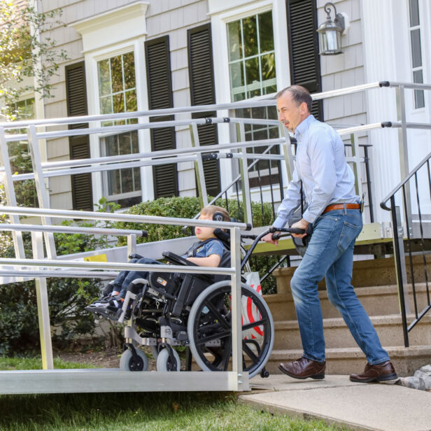 a parent pushing their child on a wheelchair up an aluminum ramp.