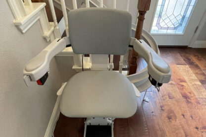 A stairlift chair installed on a residential staircase with wooden railings and leading to a closed glass-paneled door.