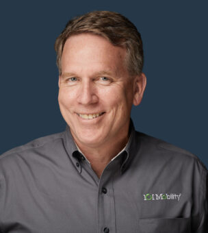 A man wearing a gray shirt with the logo "101 Mobility" smiles at the camera against a dark blue background.