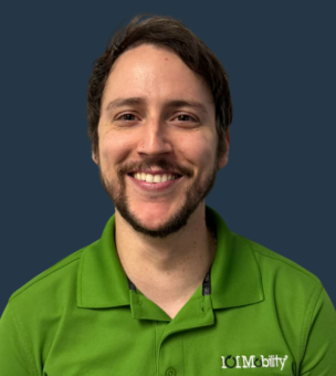 A person with short hair and a beard smiles while wearing a green polo shirt with a "101 Mobility" logo against a solid dark blue background.