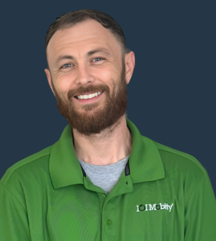 A person with short hair and a beard smiles at the camera, wearing a green polo shirt with a "101 Mobility" logo. The background is solid dark blue.