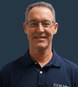 A man wearing glasses and a navy polo shirt with a logo smiles at the camera against a dark blue background.