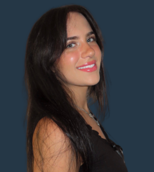 A woman with long dark hair smiles and looks over her shoulder, wearing a black top against a dark blue background.