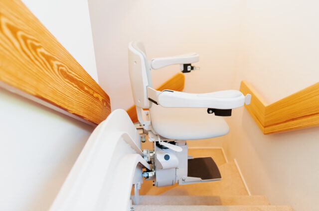 A stairlift installed on a staircase with wooden handrails, designed to assist individuals in navigating stairs.