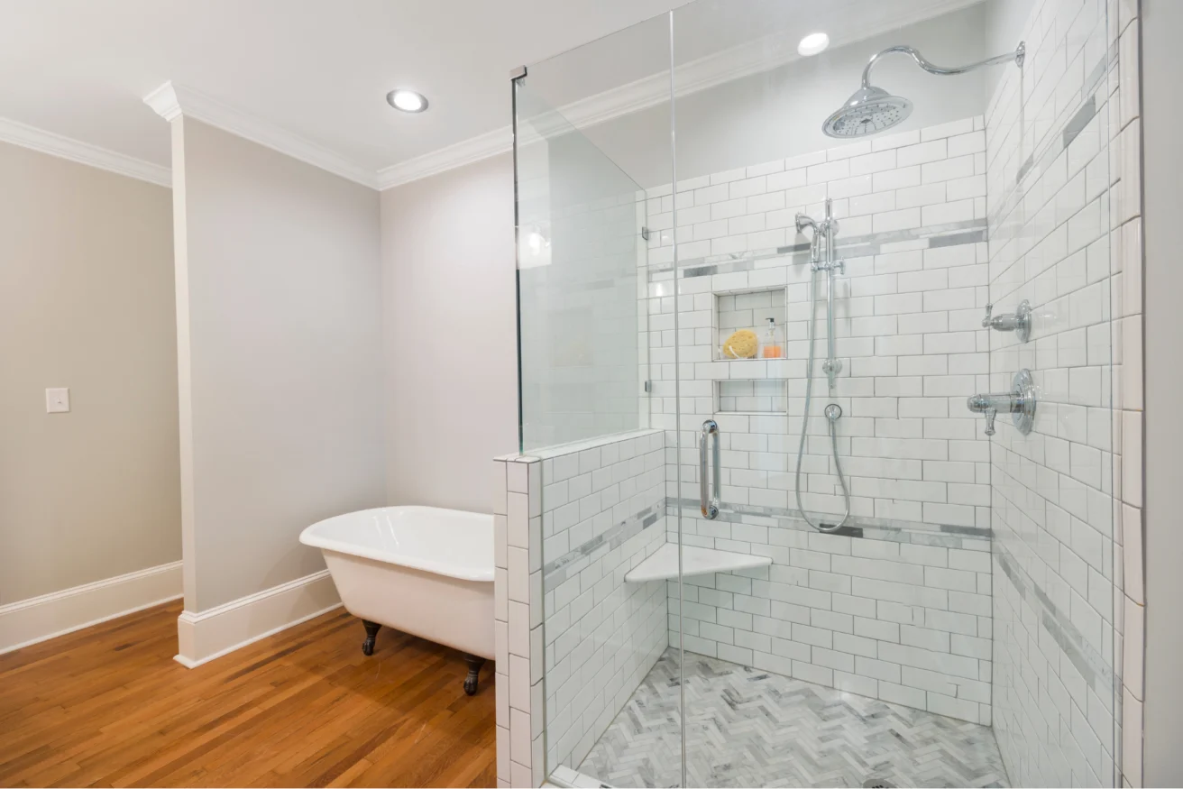 A bathroom with a clawfoot bathtub, a glass-enclosed shower with white subway tiles, and wood flooring.