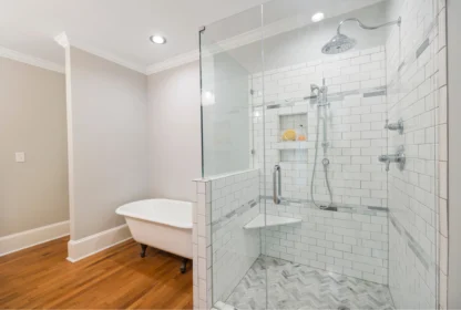 A bathroom with a clawfoot bathtub, a glass-enclosed shower with white subway tiles, and wood flooring.