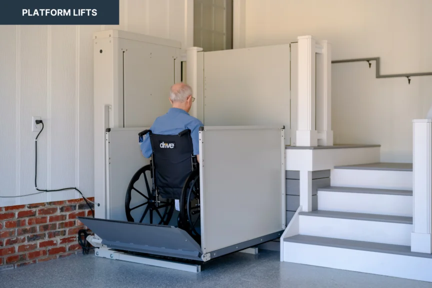 A person in a wheelchair uses a platform lift to access an elevated area next to a staircase inside a building.