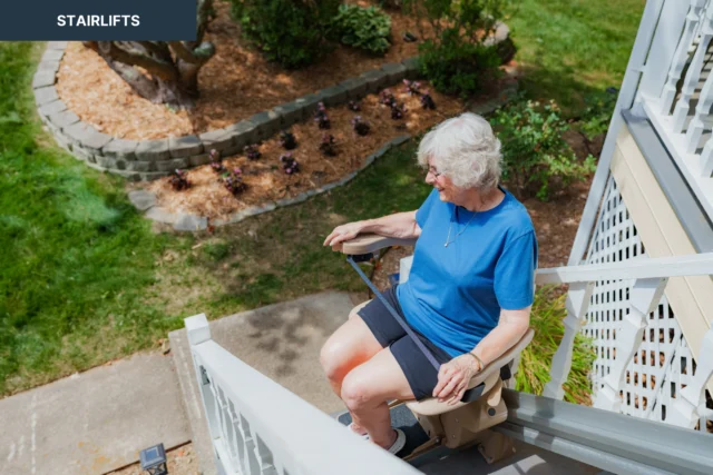 An elderly person seated on an outdoor stairlift, moving down a staircase with a garden visible in the background.