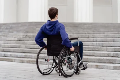 A person in a wheelchair wearing a blue hoodie is facing a staircase outdoors.