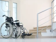 A wheelchair is positioned near a staircase in a bright, empty room.