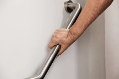 An elderly person holding onto a metal handrail attached to a white wall.