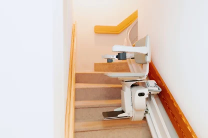 A stairlift installed on a carpeted staircase with wooden handrails.