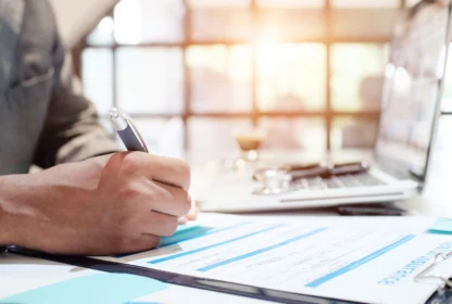 Person filling out a health insurance form at a desk with a pen, while a laptop is open nearby.