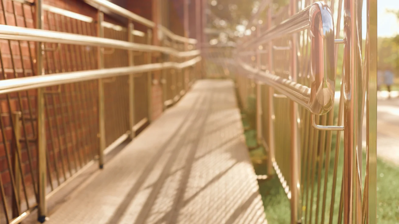 A sunlit metal accessibility ramp with railings, attached to a brick building.