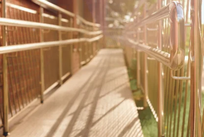 A sunlit metal accessibility ramp with railings, attached to a brick building.