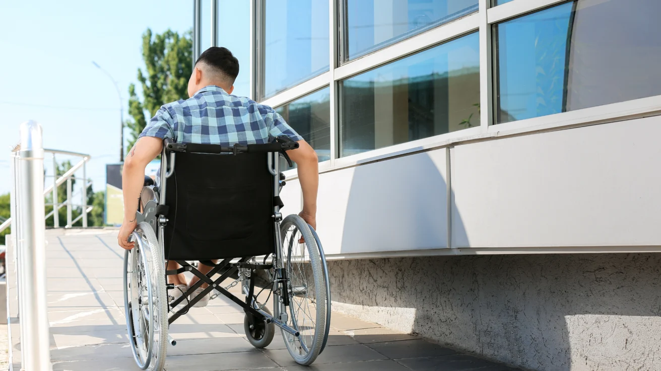 A person in a wheelchair uses a ramp outside a building.