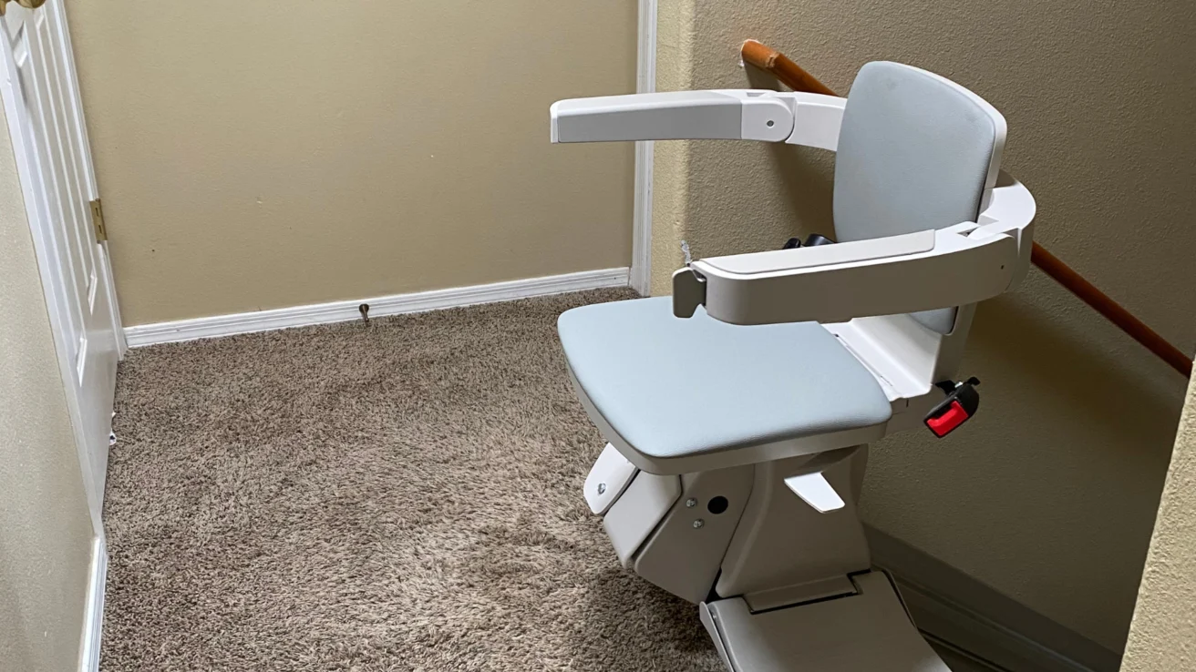 A stairlift with a cushioned seat and armrests is installed on a carpeted staircase.