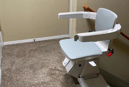 A stairlift with a cushioned seat and armrests is installed on a carpeted staircase.