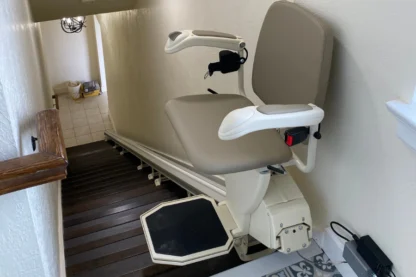 A stairlift on a residential staircase with a beige seat and armrests.