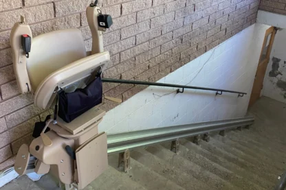 A stair lift installed on a brick wall alongside a staircase.