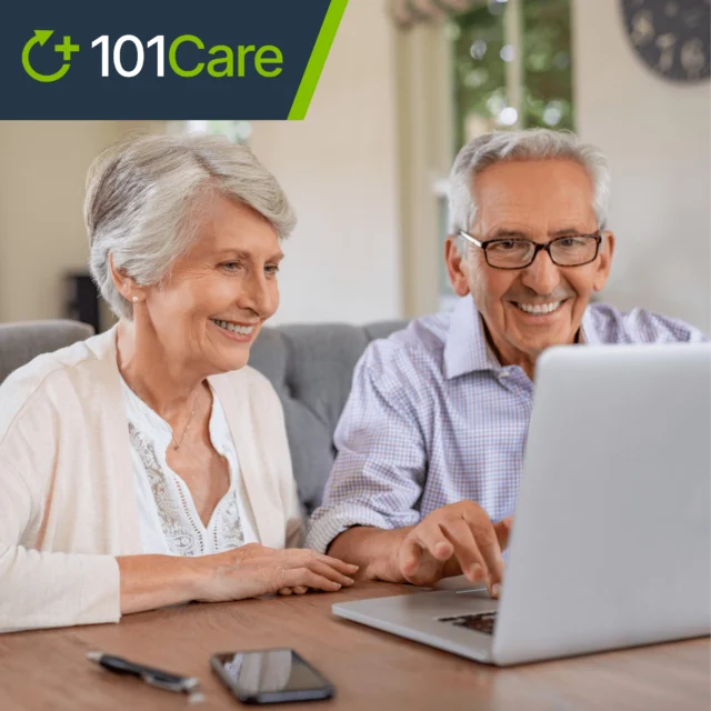 An elderly couple is smiling while looking at a laptop. A smartphone lies on the table. The image has a "101Care" logo in the top left corner.